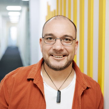 Geoffrey Campbell, smiling and standing against a modern yellow-striped wall in a professional office setting.