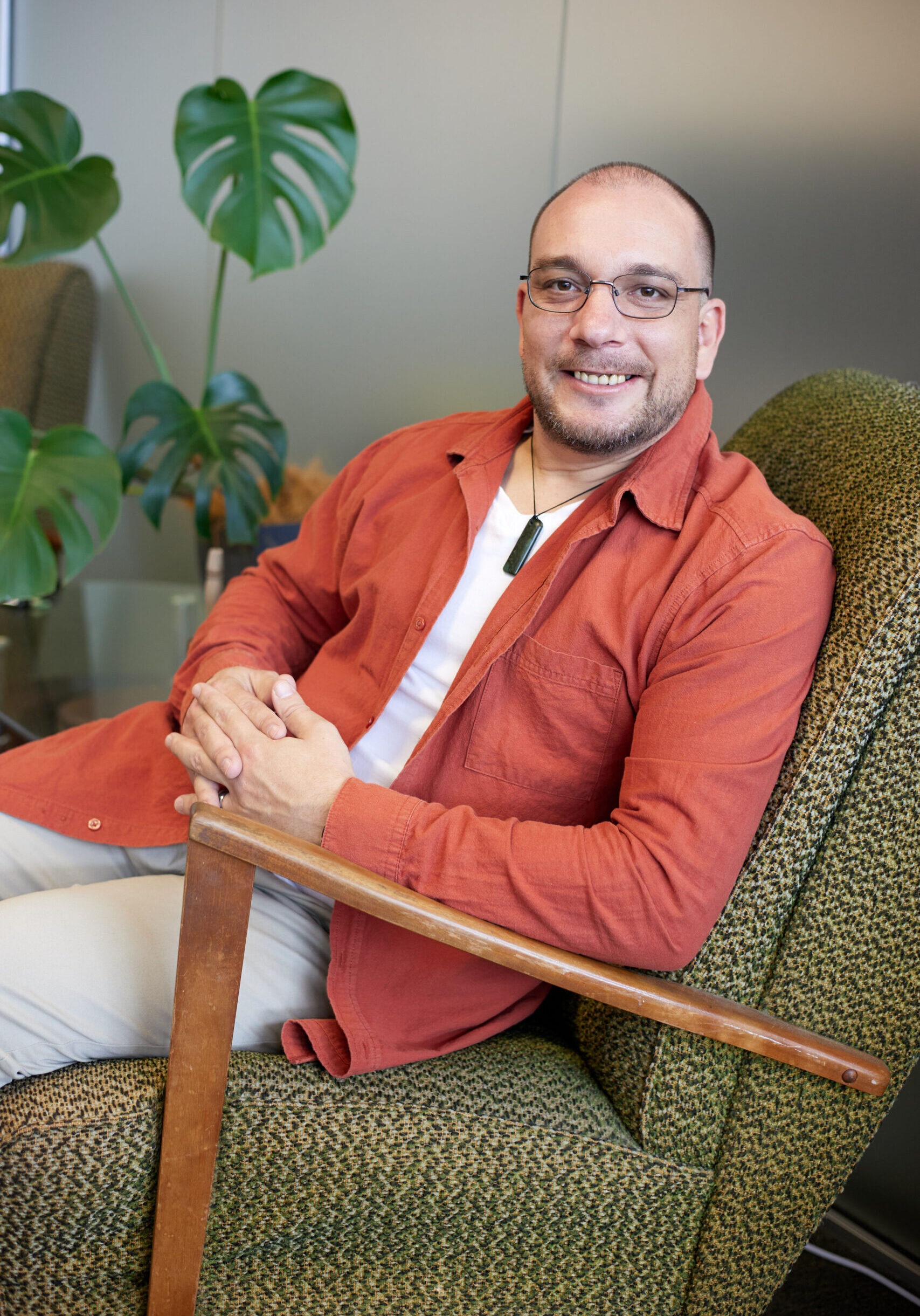 Geoffrey Campbell, seated in a green armchair, smiling confidently in a professional office setting with lush green plants in the background.